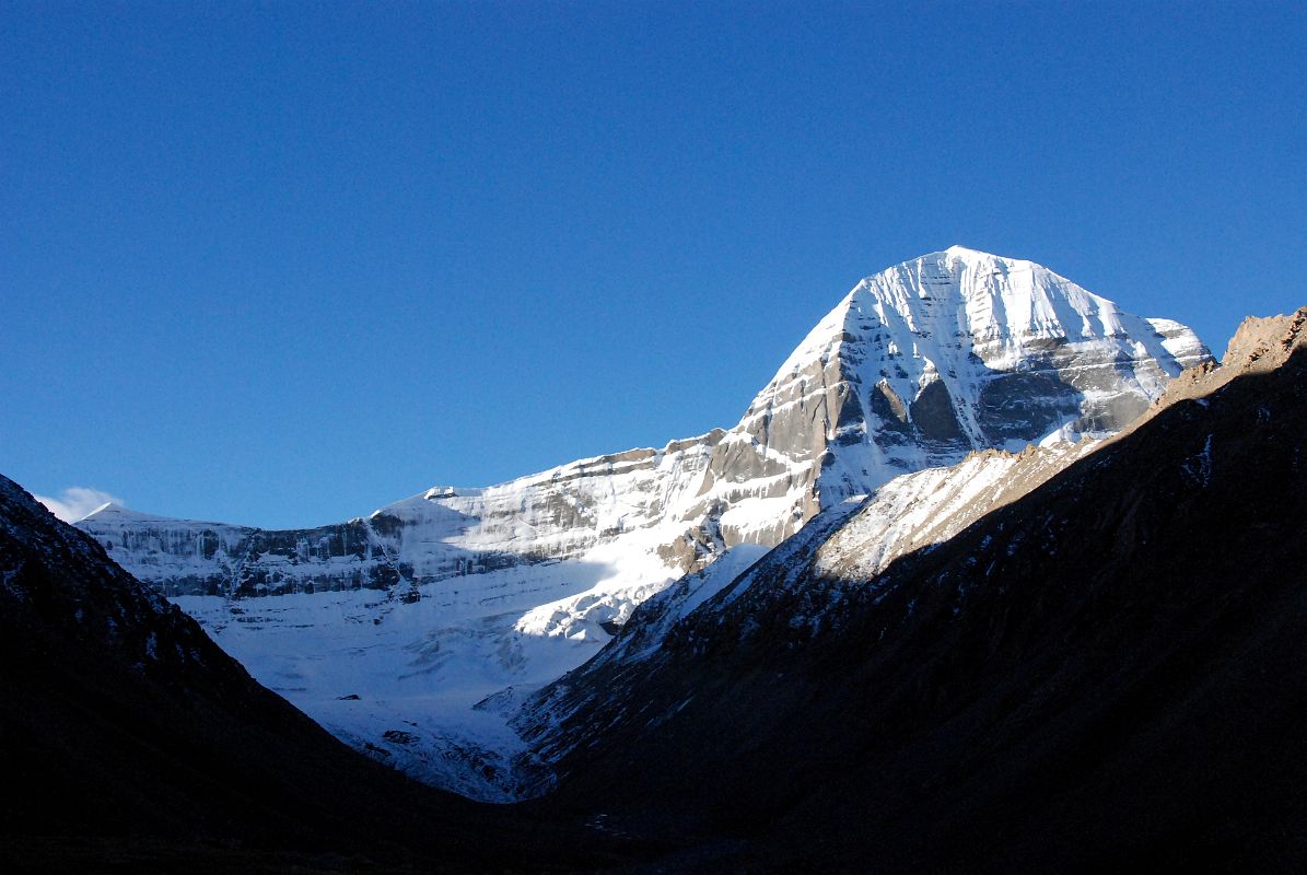 42 Mount Kailash East And North Faces And Jagged Shama Ri East Ridge From Just Beyond Dirapuk On Mount Kailash Outer Kora The trail from Dirapuk crosses a bridge and follows a broad shelf above the Dolma Chu. After only 30 minutes a perfect view of the start of the Mount Kailash East Face comes into to the east of the North Face. The north side of the sharp jagged ridge called Shama Ri, extends to the east of Mount Kailash. This ridge represents the 18 Hells: 8 Cold, 8 Hot, and 2 Trial Hells. Its treacherous appearance serves as a sober reminder to pilgrims that hell exists and perhaps looks like this. A short truncated glacier with a small but distinct terminal, lateral, and medial moraines descends from the rocky eastern arm of the east and north faces of Kailash, down through the Polung Valley between the Avalokiteshvara (Tib. Chenrezig)  and Manjushri (Tib. Jampelyang) peaks.